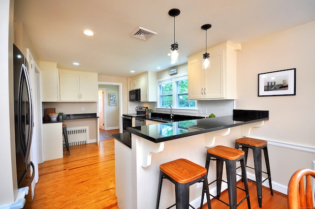 kitchen with a peninsula, stainless steel appliances, radiator, visible vents, and light wood-style flooring