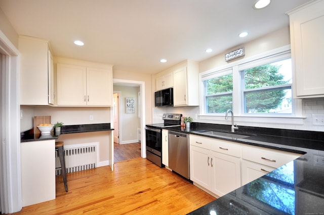 kitchen with a sink, stainless steel appliances, radiator, and white cabinetry