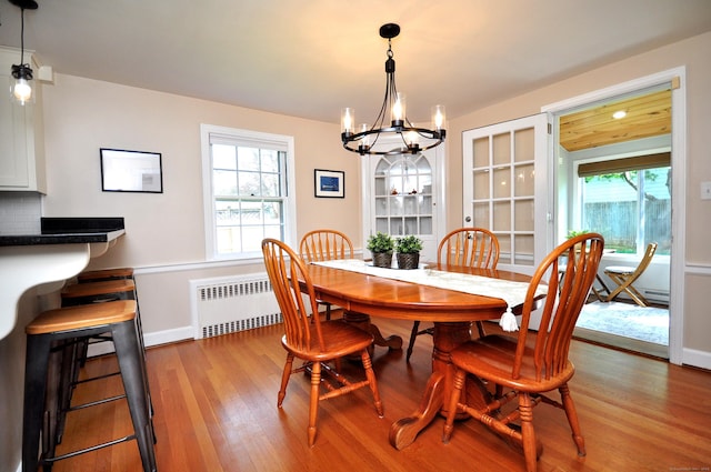 dining area featuring an inviting chandelier, baseboards, radiator heating unit, and wood finished floors