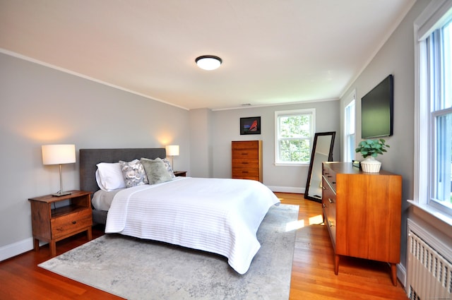 bedroom with ornamental molding, baseboards, light wood-type flooring, and radiator heating unit