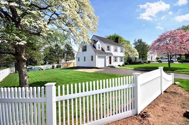 view of side of property featuring a yard, a chimney, aphalt driveway, and a fenced front yard