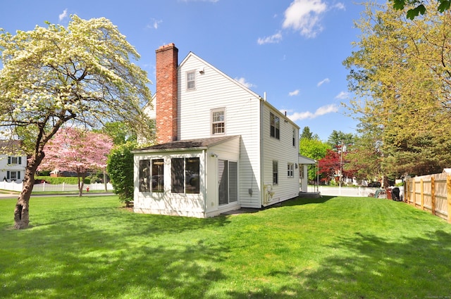 back of house featuring a chimney, a sunroom, fence, and a lawn