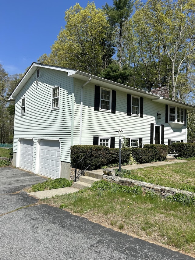 bi-level home with driveway, a chimney, and a garage