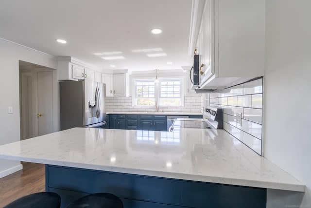 kitchen featuring a peninsula, stainless steel appliances, blue cabinetry, decorative backsplash, and ornamental molding