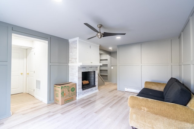 living room featuring a decorative wall, wood finished floors, visible vents, a fireplace, and ceiling fan