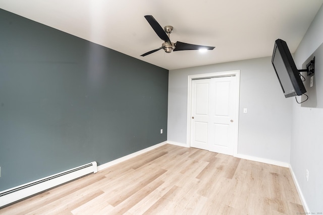 unfurnished bedroom featuring a ceiling fan, baseboard heating, a closet, baseboards, and wood finished floors