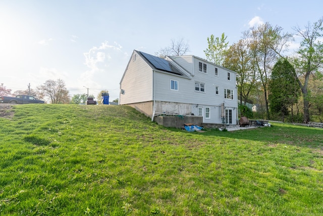 rear view of property featuring a yard, a patio, and roof mounted solar panels
