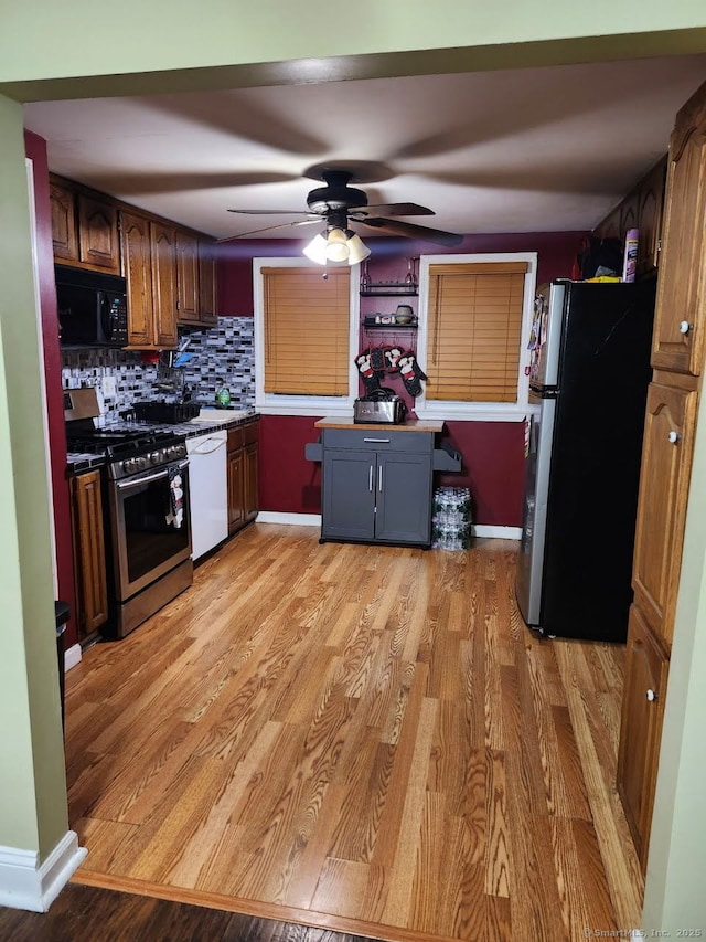kitchen with light wood-type flooring, stainless steel appliances, decorative backsplash, and a ceiling fan