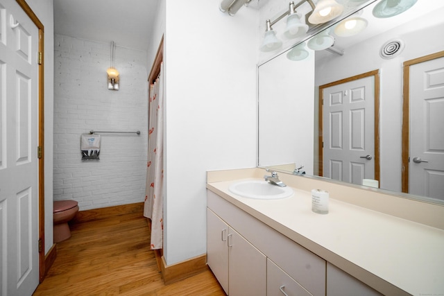 bathroom with brick wall, wood finished floors, vanity, toilet, and a shower with shower curtain