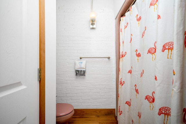 bathroom with wood finished floors, curtained shower, brick wall, and toilet