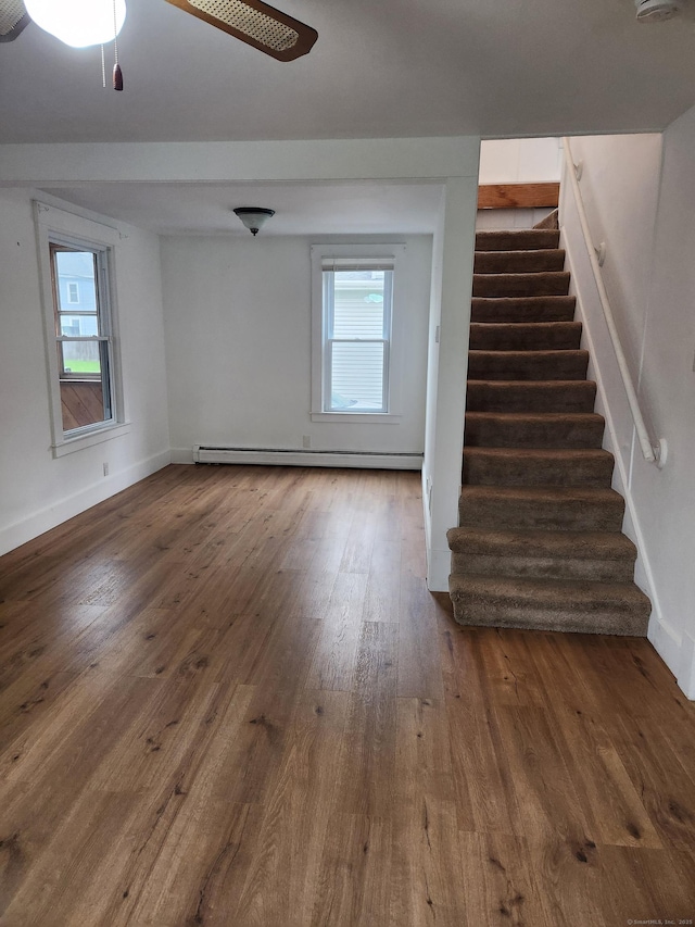 unfurnished living room with a ceiling fan, a baseboard radiator, baseboards, stairs, and hardwood / wood-style flooring