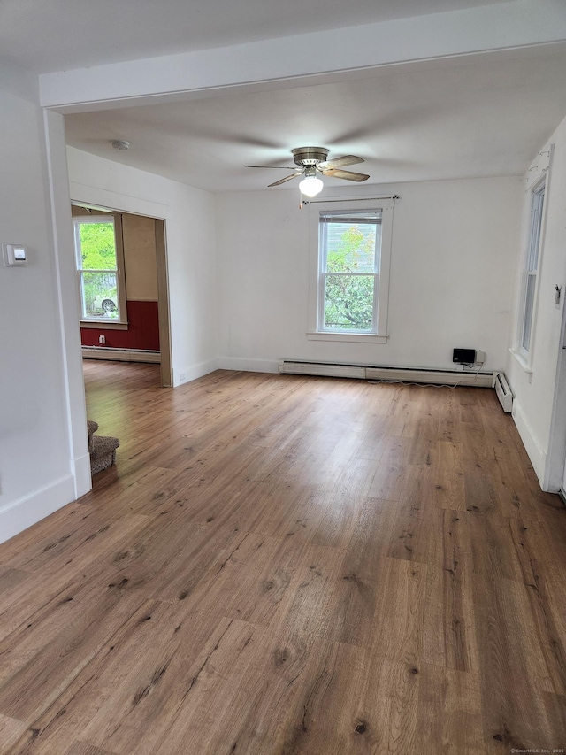 spare room featuring baseboard heating, a healthy amount of sunlight, and wood finished floors