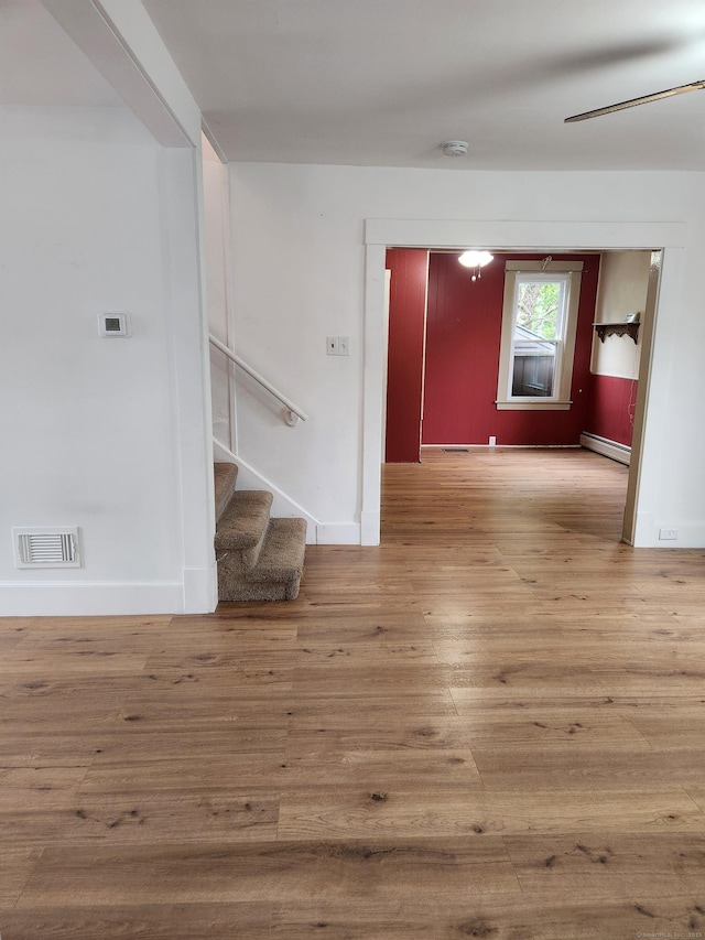 unfurnished room featuring stairs, wood finished floors, visible vents, a baseboard radiator, and baseboards