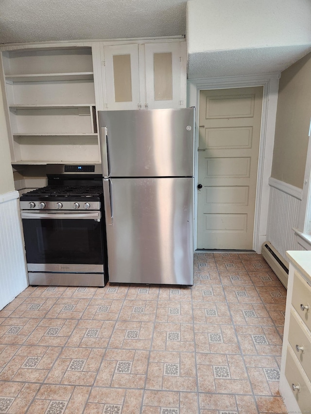 kitchen with a baseboard radiator, brick patterned floor, wainscoting, white cabinetry, and stainless steel appliances