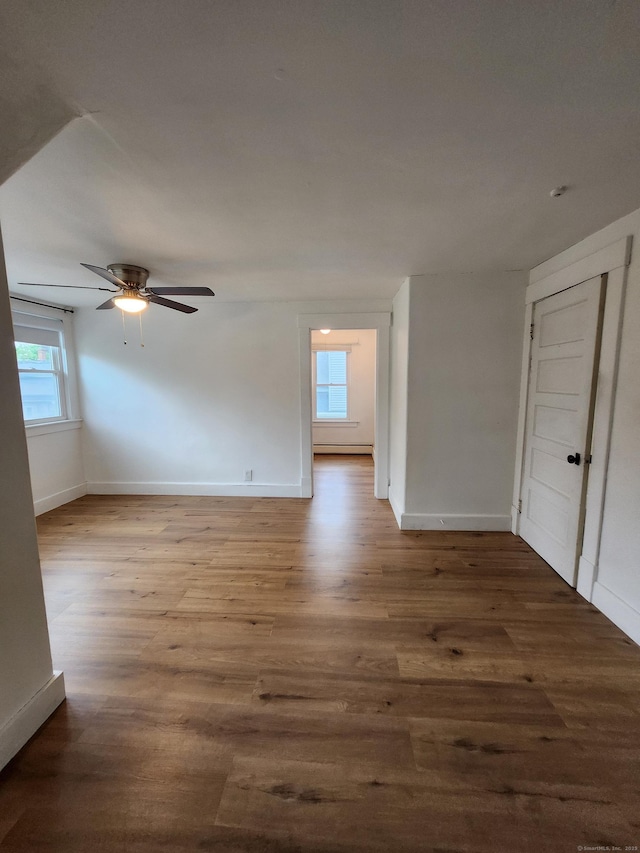 spare room with baseboards, a ceiling fan, a healthy amount of sunlight, and wood finished floors