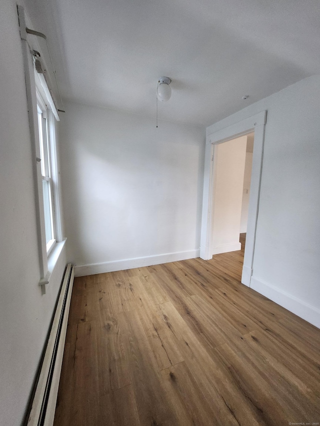empty room with baseboards, wood finished floors, and a baseboard radiator