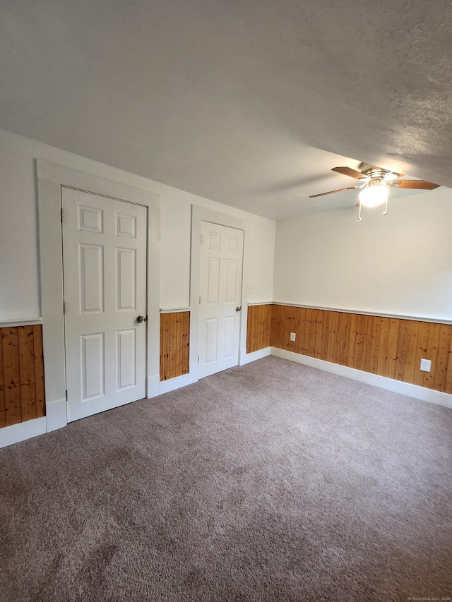 unfurnished bedroom featuring carpet flooring, wooden walls, baseboards, and wainscoting