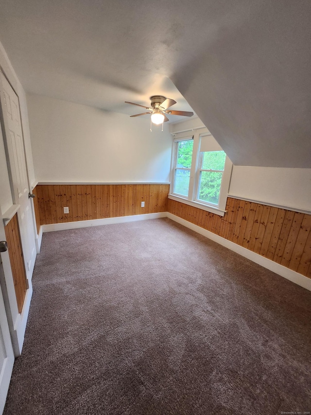 additional living space featuring a ceiling fan, carpet flooring, and wood walls