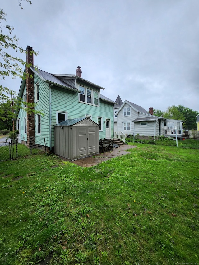 back of house featuring a storage shed, a yard, a chimney, fence, and an outbuilding