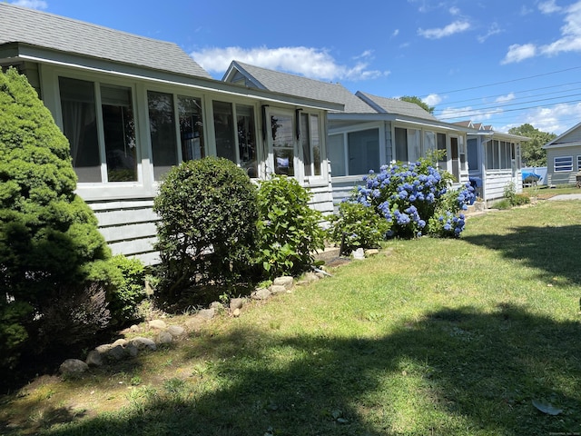exterior space with a sunroom, a shingled roof, and a yard