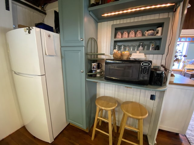 bar with freestanding refrigerator, black microwave, and dark wood-style flooring