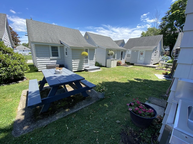 rear view of property featuring a lawn, outdoor dining area, an outdoor structure, and roof with shingles