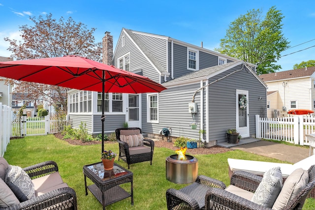 rear view of house with a gate, a patio, fence private yard, a lawn, and an outdoor living space with a fire pit