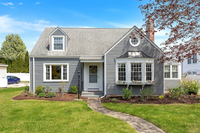 cape cod-style house featuring roof with shingles, fence, a chimney, and a front yard