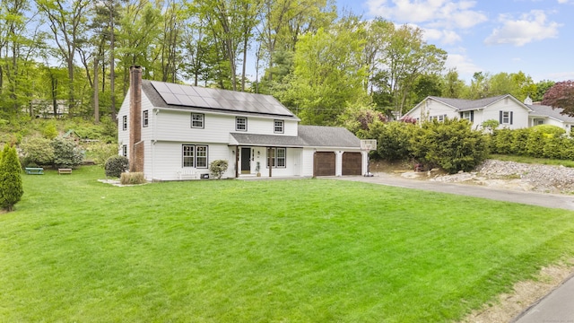 view of front of house with a garage, a chimney, roof mounted solar panels, a front lawn, and a porch