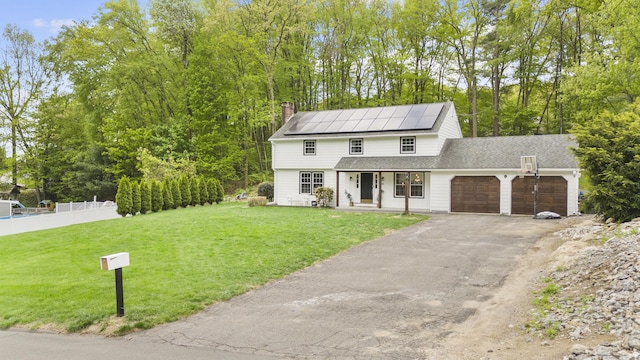 view of front of house with an attached garage, covered porch, solar panels, a chimney, and driveway