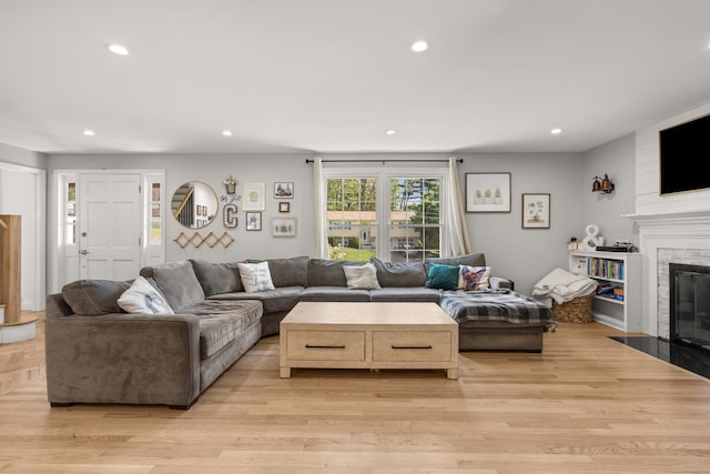 living room featuring a fireplace with flush hearth, recessed lighting, and light wood-style flooring