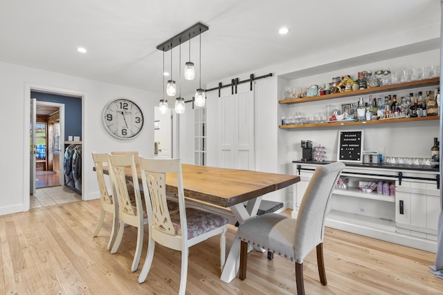 dining space featuring a barn door, washer and clothes dryer, light wood-type flooring, a dry bar, and recessed lighting