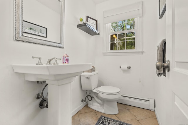 half bathroom with a baseboard heating unit, toilet, tile patterned flooring, and baseboards