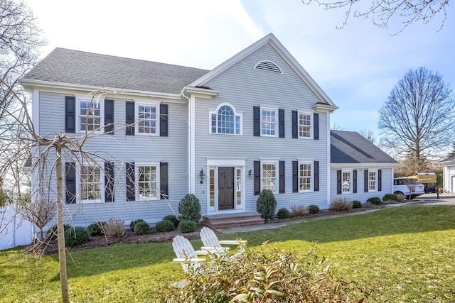 colonial-style house featuring roof with shingles and a front yard