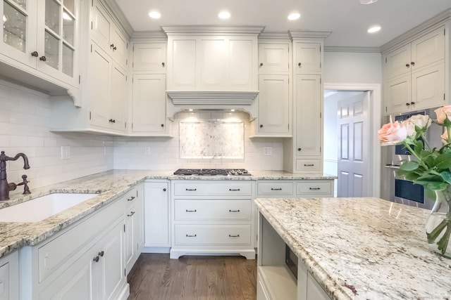 kitchen with white cabinets, light stone countertops, appliances with stainless steel finishes, a sink, and dark wood finished floors