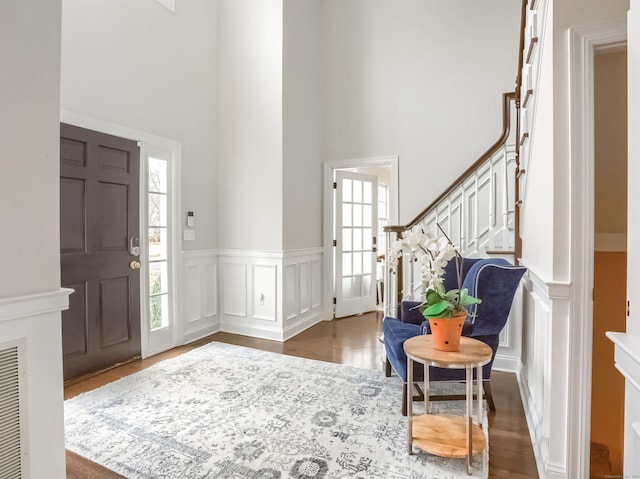 entryway with wainscoting, a high ceiling, a decorative wall, stairs, and dark wood-type flooring