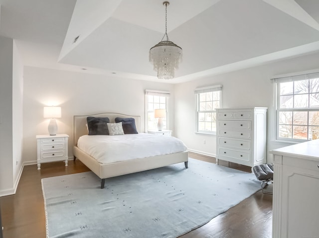 bedroom with a raised ceiling, multiple windows, a chandelier, and dark wood-type flooring
