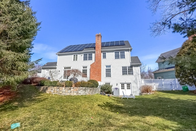 rear view of property with a lawn, fence, a chimney, and solar panels