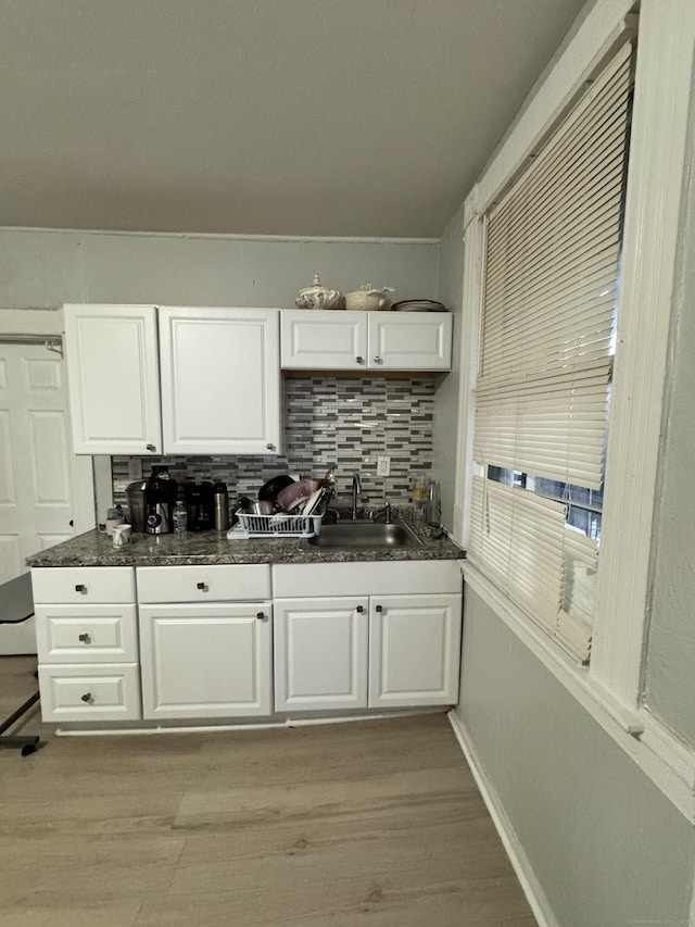 kitchen with white cabinets, dark countertops, a sink, and light wood-style floors