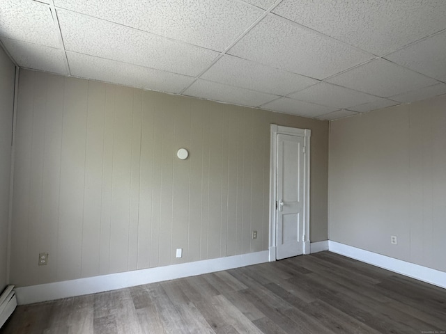 empty room with baseboards, a baseboard radiator, a drop ceiling, and wood finished floors