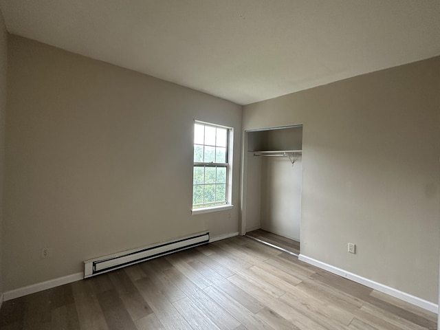 unfurnished bedroom with baseboards, wood finished floors, baseboard heating, and a closet