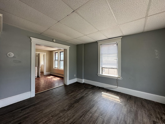 spare room featuring baseboards, a drop ceiling, and dark wood-type flooring