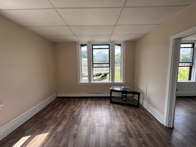 spare room with baseboards, dark wood-style flooring, a drop ceiling, and baseboard heating