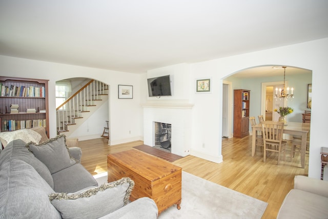 62 Lynde St, Old Saybrook, CT 06475 - living area featuring arched walkways, light wood-style flooring, a fireplace with flush hearth, a chandelier, and stairs