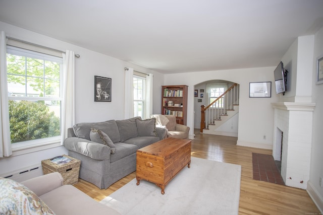 62 Lynde St, Old Saybrook, CT 06475 - living room featuring light wood finished floors, a baseboard heating unit, arched walkways, a brick fireplace, and stairway