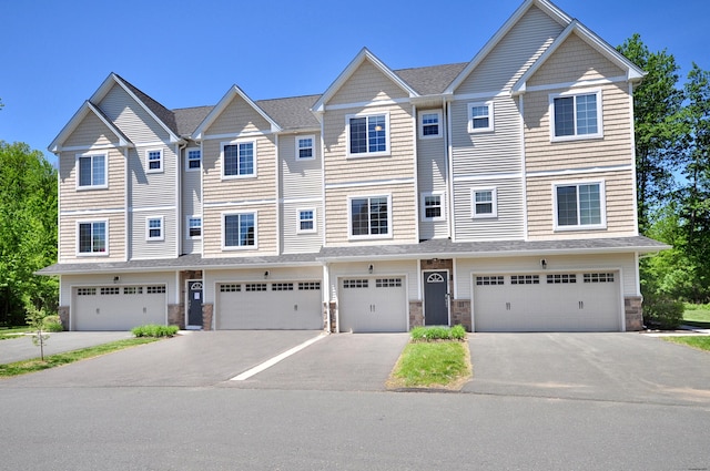 townhome / multi-family property featuring stone siding, driveway, and a garage