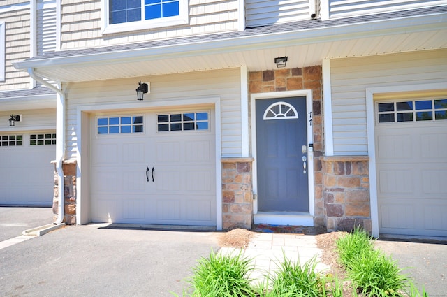 view of exterior entry featuring an attached garage, stone siding, and driveway
