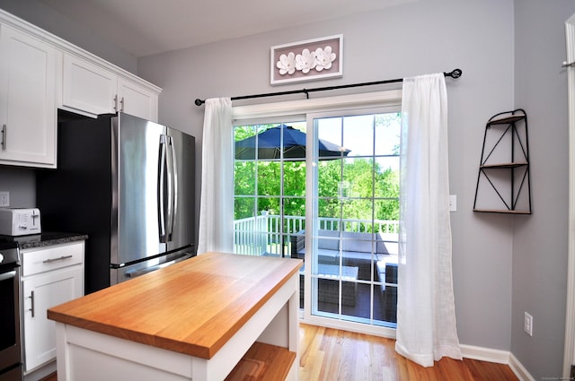 kitchen featuring freestanding refrigerator, white cabinetry, butcher block countertops, light wood-style flooring, and stove