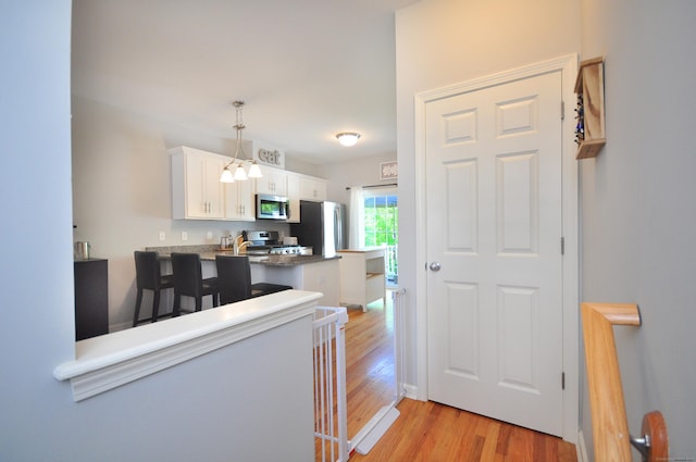 kitchen with appliances with stainless steel finishes, white cabinets, a chandelier, light wood-style floors, and a peninsula