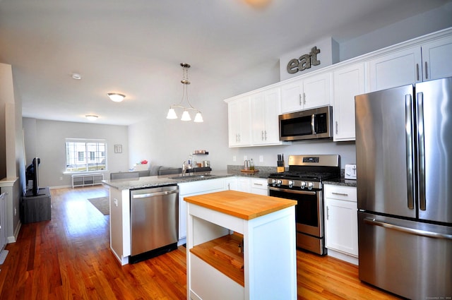 kitchen featuring appliances with stainless steel finishes, wooden counters, a peninsula, a sink, and open floor plan